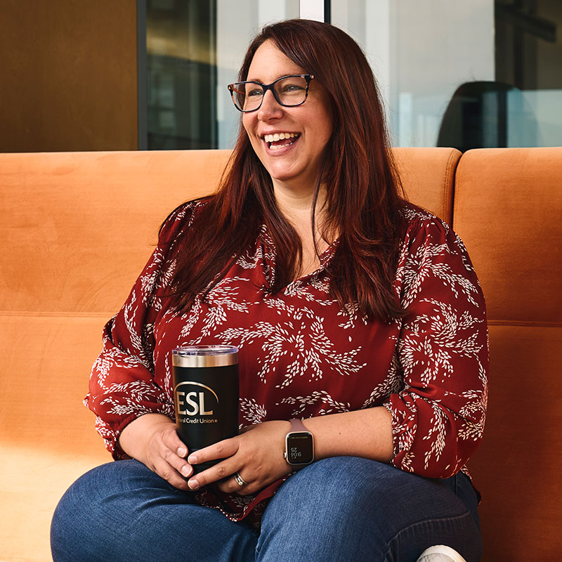 ESL employee smiling and sitting on an orange sofa holding an ESL tumbler