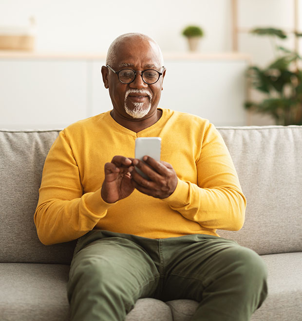 Older man sitting on couch at home looking at his cell phone.