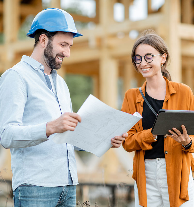 Two people reviewing blueprints and project details at a residential construction site during the home building process.