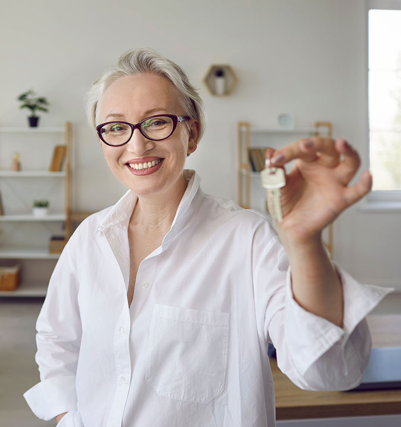 Person in a home office holding up newly received house keys, suggesting a recent purchase.