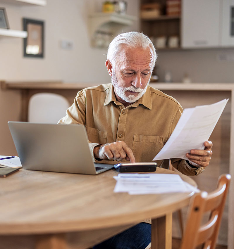 Person calculating expenses and reviewing paperwork at home, preparing finances for buying a home.