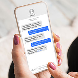 Close-up of a hand holding a phone with a thread of fake text messages designed to trick the recipient into clicking a link.
